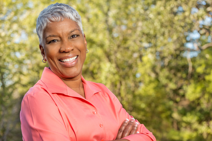 Portrait of an African American mature woman with short gray hair smiling outside with trees in the background